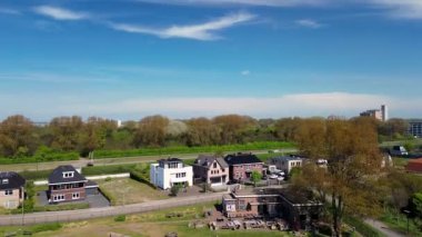 Sahil manzaralı sakin bir sahil kasabası kayalık bir kıyı şeridi, yeşil açık alanlar, geçen araçların olduğu bir yol ve açık mavi gökyüzünün altındaki konut binalarını gösteriyor. Rüzgar Değirmenleri.