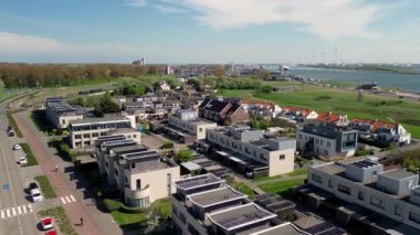 Sahil manzaralı sakin bir sahil kasabası kayalık bir kıyı şeridi, yeşil açık alanlar, geçen araçların olduğu bir yol ve açık mavi gökyüzünün altındaki konut binalarını gösteriyor. Rüzgar Değirmenleri.