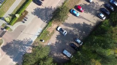 Yeşillik ve yollarla çevrili bir otoparkın hava görüntüsü, düzgün park edilmiş arabalar ve açık güneşli bir gökyüzünün altında bir inşaat alanı..