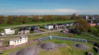 Modern binalar, ağaçlar ve yürüyüş yolları ile çevrili çimenlerle kaplı tarihi bir askeri kalenin havadan görünüşü, kıyı şeridi yakınlarında parlak mavi bir gökyüzünün altında..