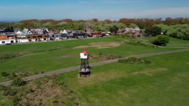 Deniz feneri, yeşil park, sahil yolu, limandaki gemiler ve arka planda rüzgar türbinleri sergilenen Hollanda kıyı kasabasının manzaralı bir manzarası..