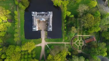 Uçsuz bucaksız yeşil tarlaları, dolambaçlı su yolları ve Hollanda 'nın düz kırsalında parçalı bulutlu bir gökyüzünün altında uzanan bir nehirle çevrili tarihi bir şatonun havadan görünüşü..