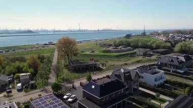 Modern binalar, ağaçlar ve yürüyüş yolları ile çevrili çimenlerle kaplı tarihi bir askeri kalenin havadan görünüşü, kıyı şeridi yakınlarında parlak mavi bir gökyüzünün altında..