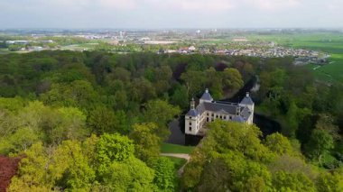 Uçsuz bucaksız yeşil tarlaları, dolambaçlı su yolları ve Hollanda 'nın düz kırsalında parçalı bulutlu bir gökyüzünün altında uzanan bir nehirle çevrili tarihi bir şatonun havadan görünüşü..