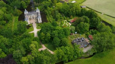 Uçsuz bucaksız yeşil tarlaları, dolambaçlı su yolları ve Hollanda 'nın düz kırsalında parçalı bulutlu bir gökyüzünün altında uzanan bir nehirle çevrili tarihi bir şatonun havadan görünüşü..