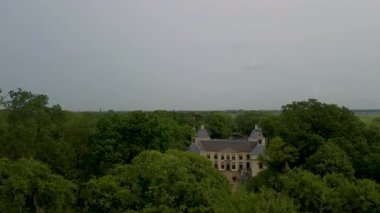 Uçsuz bucaksız yeşil tarlaları, dolambaçlı su yolları ve Hollanda 'nın düz kırsalında parçalı bulutlu bir gökyüzünün altında uzanan bir nehirle çevrili tarihi bir şatonun havadan görünüşü..