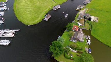 Bereketli yeşil tarlalar boyunca uzanan dar bir kanalın havadan görünüşü ve berrak mavi gökyüzünün altında limanı ve demirlemiş yatları olan huzurlu bir Hollanda köyüne uzanan küçük bir orman. Güzel bir rüzgar değirmeni.