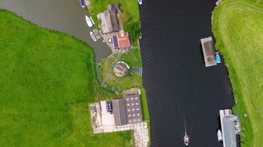 Bereketli yeşil tarlalar boyunca uzanan dar bir kanalın havadan görünüşü ve berrak mavi gökyüzünün altında limanı ve demirlemiş yatları olan huzurlu bir Hollanda köyüne uzanan küçük bir orman. Güzel bir rüzgar değirmeni.