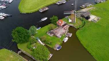 Bereketli yeşil tarlalar boyunca uzanan dar bir kanalın havadan görünüşü ve berrak mavi gökyüzünün altında limanı ve demirlemiş yatları olan huzurlu bir Hollanda köyüne uzanan küçük bir orman. Güzel bir rüzgar değirmeni.
