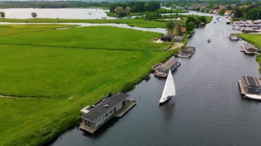 Kanal boyunca beyaz yelkenli bir yat. Güzel bir yel değirmeni. Dar bir kanalın havadan görünüşü yemyeşil çayırlarda akıyor ve küçük bir orman huzur dolu bir marinayla Hollanda köyüne gidiyor.