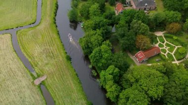 Yeşil tarlalar ve ağaçlarla çevrili dolambaçlı bir kanalı olan pitoresk bir köyün havadan görünüşü. Tekneler su boyunca demirli. Bir tekne su kanalı boyunca yol alır..
