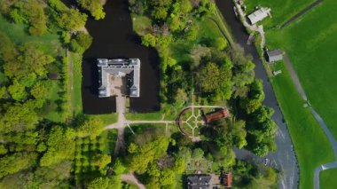 Uçsuz bucaksız yeşil tarlaları, dolambaçlı su yolları ve Hollanda 'nın düz kırsalında parçalı bulutlu bir gökyüzünün altında uzanan bir nehirle çevrili tarihi bir şatonun havadan görünüşü..