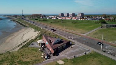 Sahil manzaralı sakin bir sahil kasabası kayalık bir kıyı şeridi, yeşil açık alanlar, geçen araçların olduğu bir yol ve açık mavi gökyüzünün altındaki konut binaları..