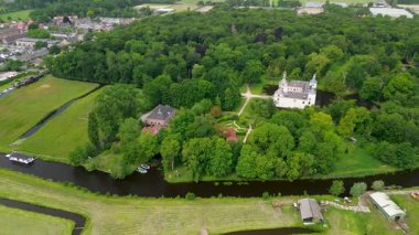 Uçsuz bucaksız yeşil tarlaları, dolambaçlı su yolları ve Hollanda 'nın düz kırsalında parçalı bulutlu bir gökyüzünün altında uzanan bir nehirle çevrili tarihi bir şatonun havadan görünüşü..