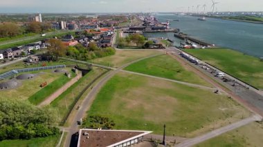 Modern binalar, ağaçlar ve yürüyüş yolları ile çevrili çimenlerle kaplı tarihi bir askeri kalenin havadan görünüşü, kıyı şeridi yakınlarında parlak mavi bir gökyüzünün altında..