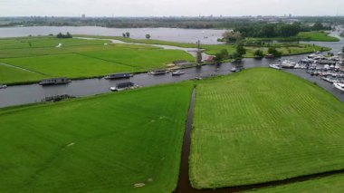 Kanal boyunca beyaz yelkenli bir yat. Güzel bir yel değirmeni. Dar bir kanalın havadan görünüşü yemyeşil çayırlarda akıyor ve küçük bir orman huzur dolu bir marinayla Hollanda köyüne gidiyor.