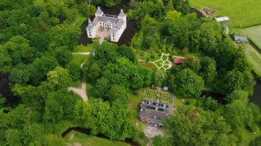 Uçsuz bucaksız yeşil tarlaları, dolambaçlı su yolları ve Hollanda 'nın düz kırsalında parçalı bulutlu bir gökyüzünün altında uzanan bir nehirle çevrili tarihi bir şatonun havadan görünüşü..