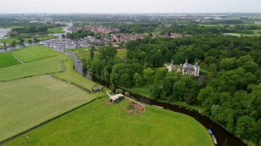 Uçsuz bucaksız yeşil tarlaları, dolambaçlı su yolları ve Hollanda 'nın düz kırsalında parçalı bulutlu bir gökyüzünün altında uzanan bir nehirle çevrili tarihi bir şatonun havadan görünüşü..