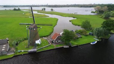 Bereketli yeşil tarlalar boyunca uzanan dar bir kanalın havadan görünüşü ve berrak mavi gökyüzünün altında limanı ve demirlemiş yatları olan huzurlu bir Hollanda köyüne uzanan küçük bir orman. Güzel bir rüzgar değirmeni.