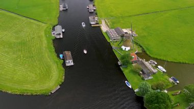 Kanal boyunca beyaz yelkenli bir yat. Güzel bir yel değirmeni. Dar bir kanalın havadan görünüşü yemyeşil çayırlarda akıyor ve küçük bir orman huzur dolu bir marinayla Hollanda köyüne gidiyor.