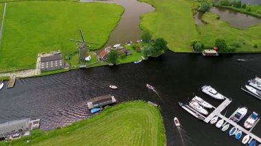 Kanal boyunca beyaz yelkenli bir yat. Güzel bir yel değirmeni. Dar bir kanalın havadan görünüşü yemyeşil çayırlarda akıyor ve küçük bir orman huzur dolu bir marinayla Hollanda köyüne gidiyor.