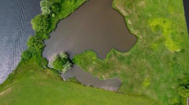 Bereketli yeşil çimenler ve dağınık ağaçlarla çevrili sakin bir nehir kıvrımının havadan görünüşü. Su doğal bir eğri oluşturur ve karayla akan nehir arasında barışçıl bir kontrastlık yaratır. Göl.