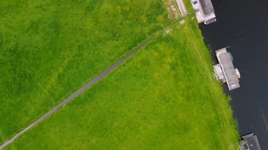 Bereketli yeşil tarlalar boyunca uzanan dar bir kanalın havadan görünüşü ve berrak mavi gökyüzünün altında limanı ve demirlemiş yatları olan huzurlu bir Hollanda köyüne uzanan küçük bir orman. Güzel bir rüzgar değirmeni.