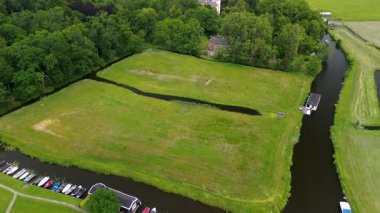 Uçsuz bucaksız yeşil tarlaları, dolambaçlı su yolları ve Hollanda 'nın düz kırsalında parçalı bulutlu bir gökyüzünün altında uzanan bir nehirle çevrili tarihi bir şatonun havadan görünüşü..