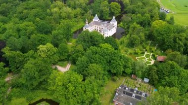 Uçsuz bucaksız yeşil tarlaları, dolambaçlı su yolları ve Hollanda 'nın düz kırsalında parçalı bulutlu bir gökyüzünün altında uzanan bir nehirle çevrili tarihi bir şatonun havadan görünüşü..