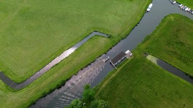 Ahşap rıhtımlar boyunca kenetlenmiş bir marina manzarası, yeşil parklar ve doğal otlaklarla çevrili dar bir su yolunda seyreden bir tekne..