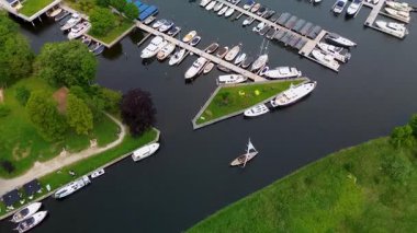 Kanal boyunca beyaz yelkenli bir yat. Güzel bir yel değirmeni. Dar bir kanalın havadan görünüşü yemyeşil çayırlarda akıyor ve küçük bir orman huzur dolu bir marinayla Hollanda köyüne gidiyor.