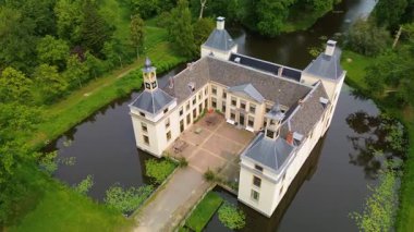 Uçsuz bucaksız yeşil tarlaları, dolambaçlı su yolları ve Hollanda 'nın düz kırsalında parçalı bulutlu bir gökyüzünün altında uzanan bir nehirle çevrili tarihi bir şatonun havadan görünüşü..