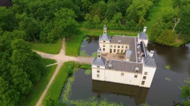 Uçsuz bucaksız yeşil tarlaları, dolambaçlı su yolları ve Hollanda 'nın düz kırsalında parçalı bulutlu bir gökyüzünün altında uzanan bir nehirle çevrili tarihi bir şatonun havadan görünüşü..