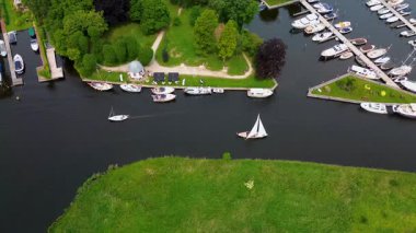 Kanal boyunca beyaz yelkenli bir yat. Güzel bir yel değirmeni. Dar bir kanalın havadan görünüşü yemyeşil çayırlarda akıyor ve küçük bir orman huzur dolu bir marinayla Hollanda köyüne gidiyor.