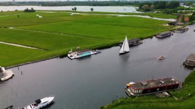 Kanal boyunca beyaz yelkenli bir yat. Güzel bir yel değirmeni. Dar bir kanalın havadan görünüşü yemyeşil çayırlarda akıyor ve küçük bir orman huzur dolu bir marinayla Hollanda köyüne gidiyor.