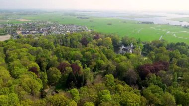 Uçsuz bucaksız yeşil tarlaları, dolambaçlı su yolları ve Hollanda 'nın düz kırsalında parçalı bulutlu bir gökyüzünün altında uzanan bir nehirle çevrili tarihi bir şatonun havadan görünüşü..