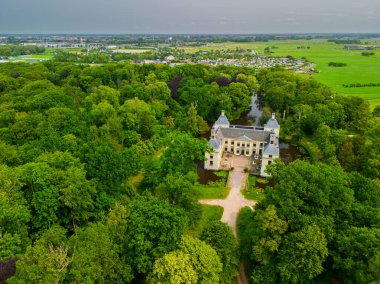 Uçsuz bucaksız yeşil tarlaları, dolambaçlı su yolları ve Hollanda 'nın düz kırsalında parçalı bulutlu bir gökyüzünün altında uzanan bir nehirle çevrili tarihi bir şatonun havadan görünüşü..