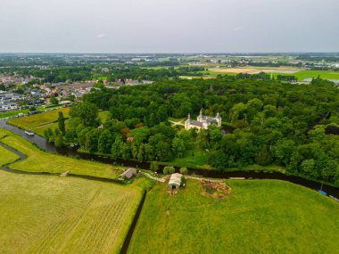 Uçsuz bucaksız yeşil tarlaları, dolambaçlı su yolları ve Hollanda 'nın düz kırsalında parçalı bulutlu bir gökyüzünün altında uzanan bir nehirle çevrili tarihi bir şatonun havadan görünüşü..