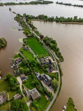 Dar yarımadaları, yeşil tarlaları ve Hollanda kırsalında bulutlu bir gökyüzünün altında sakin sularla çevrili evleri olan manzaralı göl manzaralı bir köy..