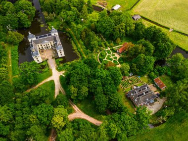 Uçsuz bucaksız yeşil tarlaları, dolambaçlı su yolları ve Hollanda 'nın düz kırsalında parçalı bulutlu bir gökyüzünün altında uzanan bir nehirle çevrili tarihi bir şatonun havadan görünüşü..
