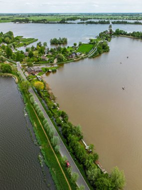 Dar yarımadaları, yeşil tarlaları ve Hollanda kırsalında bulutlu bir gökyüzünün altında sakin sularla çevrili evleri olan manzaralı göl manzaralı bir köy..