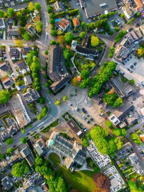 Zengin yeşillik, antika evler ve park halindeki arabalarla çevrili uzun yeşil bir kuleye sahip seçkin bir kilisenin yer aldığı pitoresk bir Avrupa kasabasının havadan görünüşü..