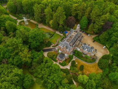 Etrafı yemyeşil ağaçlarla çevrili tarihi bir malikanenin havadan görünüşü ve çeşmesi, yürüyüş yolları ve park yeri olan güzel manzaralı bir bahçe. Sahne canlı yaz yeşilliklerini gösteriyor..