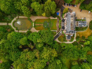 Etrafı yemyeşil ağaçlarla çevrili tarihi bir malikanenin havadan görünüşü ve çeşmesi, yürüyüş yolları ve park yeri olan güzel manzaralı bir bahçe. Sahne canlı yaz yeşilliklerini gösteriyor..