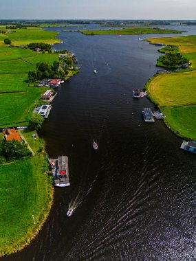 Ahşap rıhtımlar boyunca kenetlenmiş bir marina manzarası, yeşil parklar ve doğal otlaklarla çevrili dar bir su yolunda seyreden bir tekne..