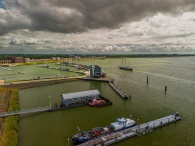 Virajlı rıhtımlar boyunca kenetlenmiş yatları olan modern bir marinanın havadan görünüşü. Limanın çevresinde yeşil çatıları, açık meydanları ve rıhtıma yakın park alanları olan konut binaları bulunuyor..