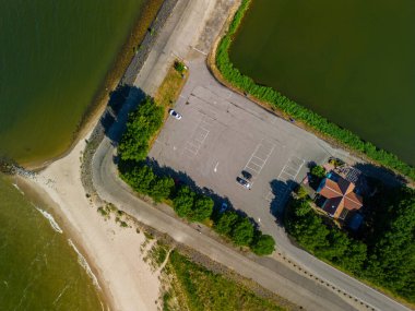 Dar bir barajın ya da dar bir geçidin havadan görünüşü her iki taraftaki geniş su kütleleri tarafından çevrelenmiş, dağınık bulutlarla dolu canlı mavi bir gökyüzünün altında ufka doğru yol alıyor..