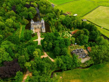 Uçsuz bucaksız yeşil tarlaları, dolambaçlı su yolları ve Hollanda 'nın düz kırsalında parçalı bulutlu bir gökyüzünün altında uzanan bir nehirle çevrili tarihi bir şatonun havadan görünüşü..