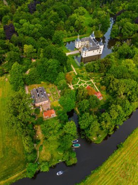 Uçsuz bucaksız yeşil tarlaları, dolambaçlı su yolları ve Hollanda 'nın düz kırsalında parçalı bulutlu bir gökyüzünün altında uzanan bir nehirle çevrili tarihi bir şatonun havadan görünüşü..