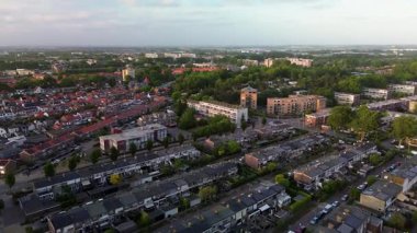 Yeşil yemyeşil evlerle çevrili banliyö mahallesinin havadan görünüşü, bir ormanın yakınında, bulutlu bir gökyüzünün altında şehrin ufuk çizgisi görünür..